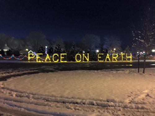 A snowy scene at night featuring illuminated letters that read "PEACE ON EARTH" surrounded by festive lights.