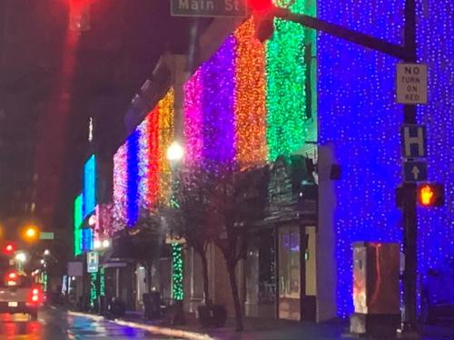 Colorful holiday lights adorn buildings along a street at night, reflecting a festive atmosphere.