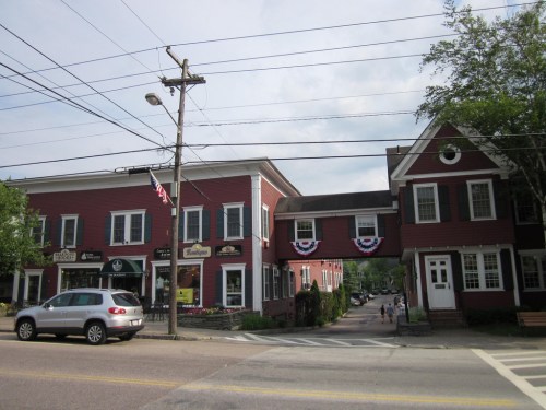 A quaint street scene featuring red buildings with decorative flags and a pedestrian bridge connecting them.