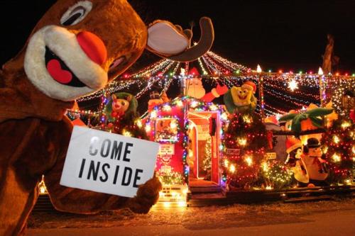 A festive reindeer mascot holds a sign reading "Come Inside" in front of a brightly lit holiday display.