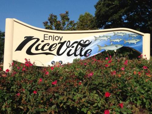 Sign reading "Enjoy Niceville" with fish illustrations and surrounded by colorful flowers.