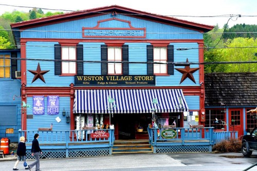 Colorful blue building with a sign reading "Weston Village Store," featuring striped awnings and a welcoming entrance.