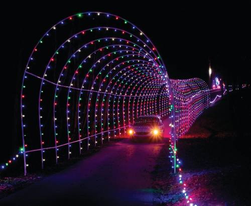A car drives through a colorful, illuminated tunnel of lights at night, creating a festive atmosphere.