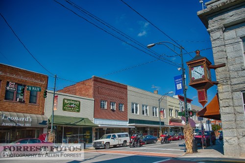 A charming small-town street with shops, a clock tower, and clear blue skies.
