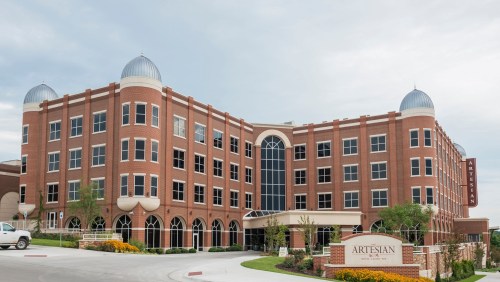 A large brick building with domed roofs and large windows, featuring a sign that reads "Artesian."