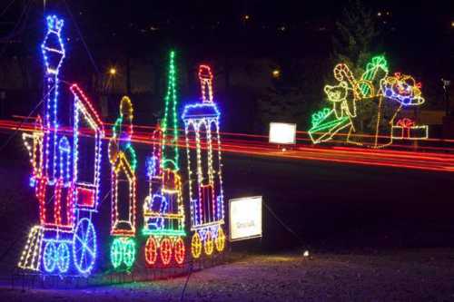 Colorful holiday lights depict a train and a gift, creating a festive nighttime scene.