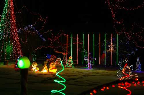 Colorful holiday lights illuminate a snowy landscape, featuring trees, decorations, and festive figures.