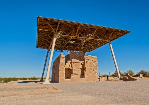 Ancient ruins sheltered under a modern canopy, set against a clear blue sky in a desert landscape.