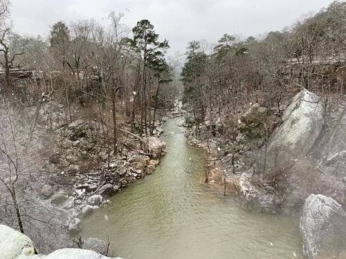 A snowy landscape featuring a winding river surrounded by trees and rocky terrain.