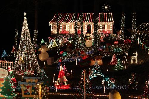A festive display of colorful Christmas lights featuring a decorated house, trees, snowmen, and various holiday decorations.