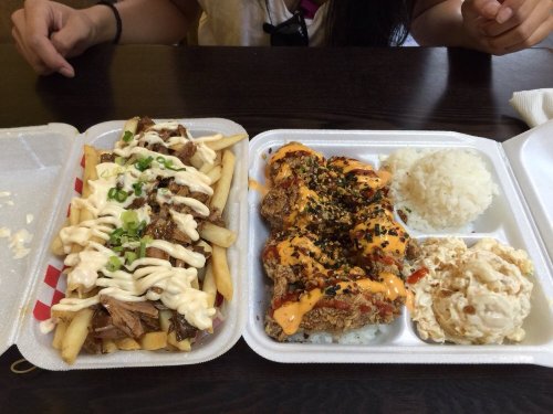 A takeout meal featuring fries topped with meat and sauce, fried chicken with spicy sauce, rice, and a side salad.