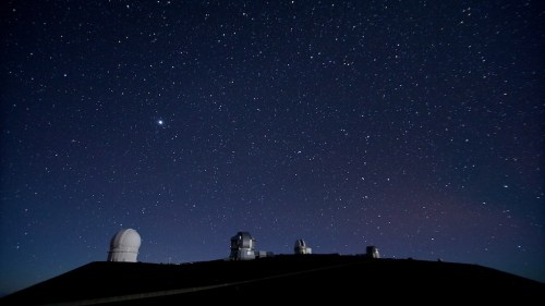 A clear night sky filled with stars above observatories on a hilltop.