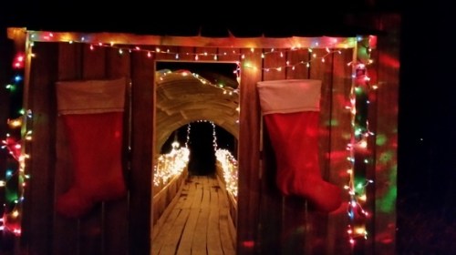 A festive wooden archway decorated with colorful lights and large red Christmas stockings.