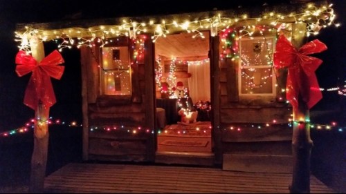 A cozy cabin decorated with colorful lights and bows, glowing warmly at night.