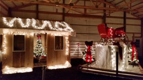 A festive scene featuring a lit wooden cabin, a decorated Christmas tree, and a sleigh adorned with lights and bows.