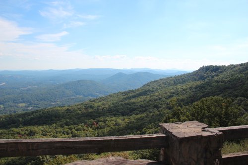 A scenic view of rolling green mountains under a blue sky, with a stone railing in the foreground.