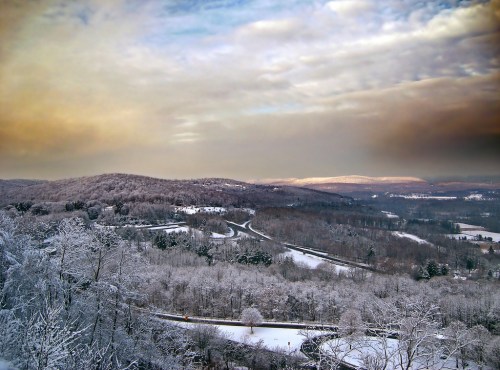 A snowy landscape with rolling hills, winding roads, and a cloudy sky at dusk.