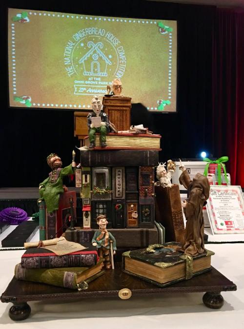 A creative gingerbread house display featuring whimsical characters and books, set against a festive backdrop.