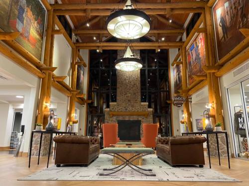 Cozy lodge interior with wooden beams, large paintings, a stone fireplace, and comfortable seating.
