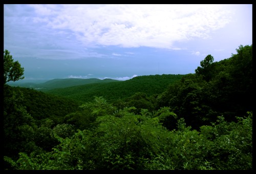 Lush green hills under a cloudy sky, with layers of mountains fading into the distance.