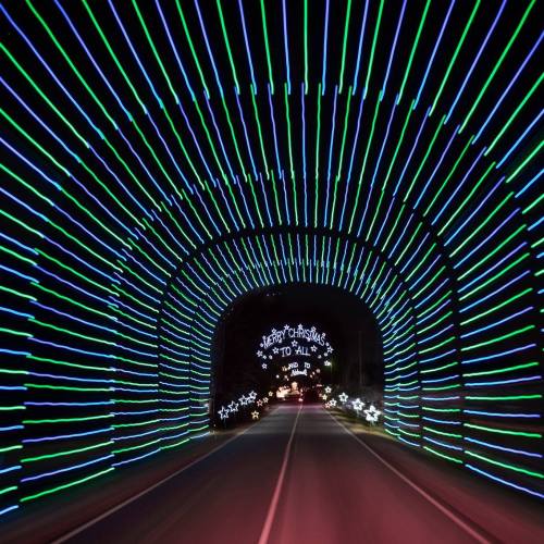 A brightly lit tunnel of green and blue lights with a "Merry Christmas to All" sign at the end.
