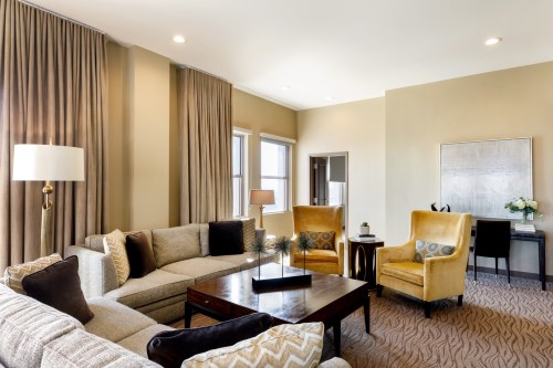 A stylish living room featuring a beige sofa, yellow armchairs, a coffee table, and large windows with curtains.