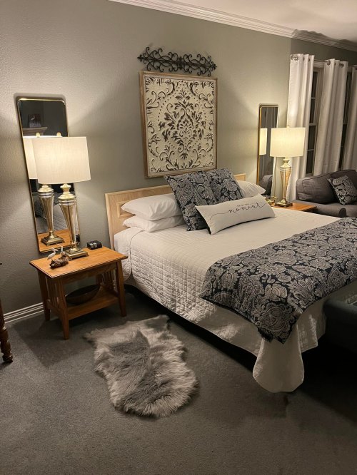 Cozy bedroom with a bed, decorative pillows, two lamps, a nightstand, and a soft rug on the floor.