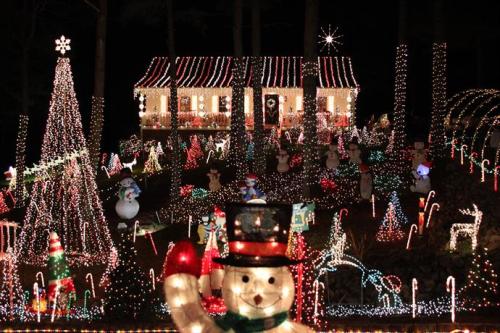 A festive house decorated with colorful Christmas lights, snowmen, candy canes, and a large illuminated tree.