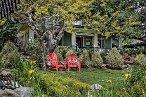 A charming house with a green exterior, surrounded by lush gardens and two red chairs in the foreground.