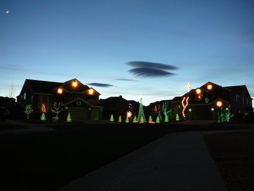 Two houses decorated with colorful holiday lights against a twilight sky, featuring trees and festive designs.