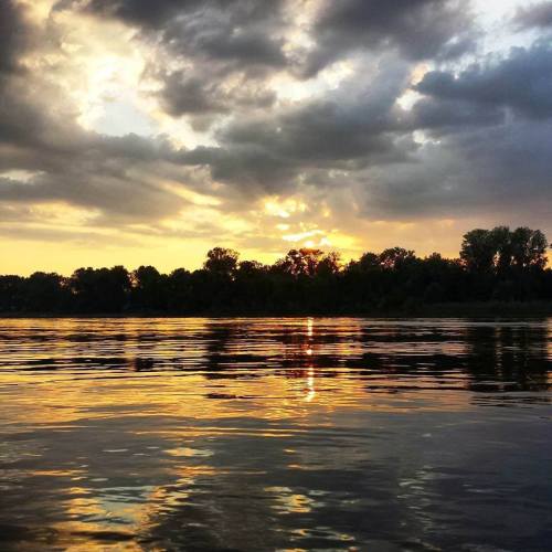A serene sunset over a calm river, with vibrant colors reflecting on the water and clouds in the sky.
