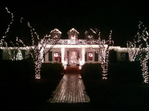 A beautifully decorated house at night, adorned with festive lights and wreaths, surrounded by illuminated trees.
