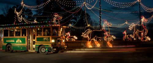 A festive trolley decorated with lights, surrounded by illuminated reindeer and holiday decorations at dusk.