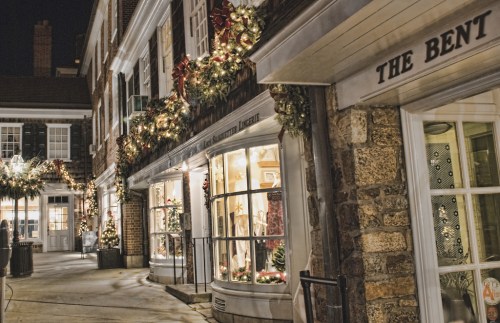 A charming street at night, adorned with festive holiday decorations and lights on the storefronts.