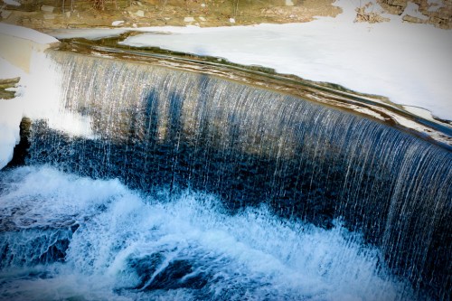 A waterfall cascading over a frozen edge, with icy surroundings and shimmering water below.