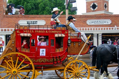 A colorful stagecoach with passengers, including a child, rides through a festive street during a parade.