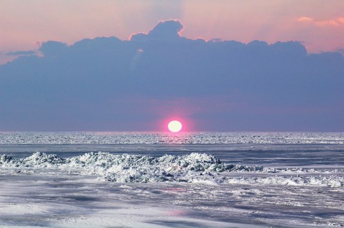 A serene sunset over a calm ocean, with soft waves and a colorful sky filled with clouds.