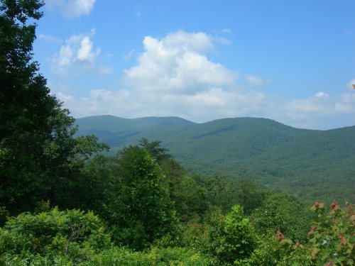 Lush green mountains under a blue sky with fluffy clouds, showcasing a serene natural landscape.