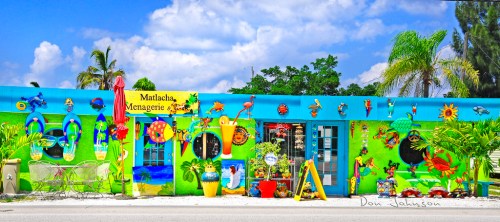 Colorful storefront with vibrant murals, tropical decorations, and plants under a bright blue sky.