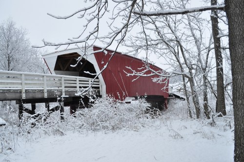 A red covered bridge surrounded by snow-covered trees and a winter landscape.