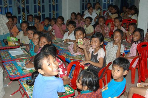 A lively group of children smiling and sitting at tables in a classroom, engaged and enjoying their time together.