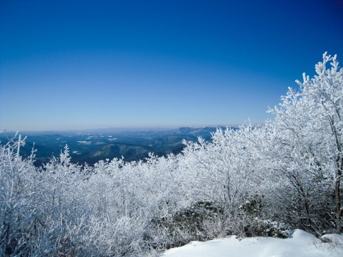 A snowy landscape with frosted trees under a clear blue sky, showcasing distant mountains and a serene winter scene.