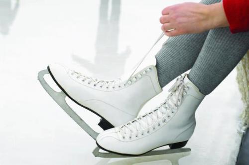 A person tying the laces of a white ice skate while sitting on the ice rink.
