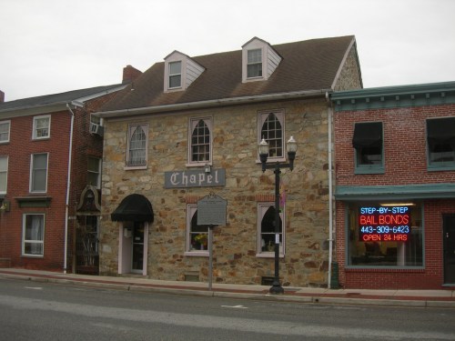 A stone building labeled "Chapel" next to a brightly lit bail bonds shop, with a cloudy sky overhead.