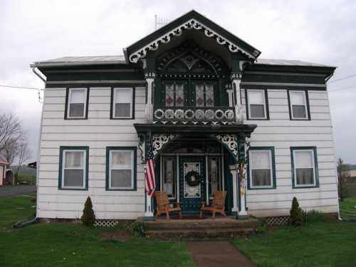 A two-story Victorian-style house with intricate woodwork, a porch, and an American flag in front.