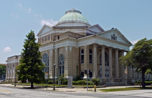 Historic building with a large dome, columns, and decorative architecture, surrounded by trees and a clear blue sky.