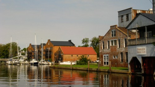 A serene waterfront scene featuring boats, historic buildings, and calm water reflecting the sky.