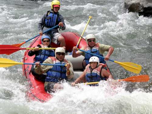 A group of five people in a red raft navigating whitewater rapids, wearing helmets and life jackets.