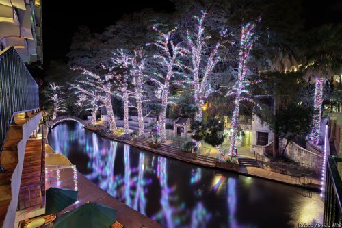 A serene night scene of a river lined with trees adorned in colorful lights, reflecting on the water's surface.