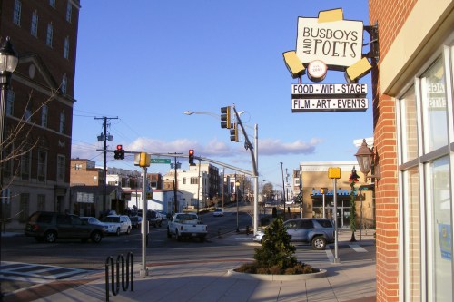 Street view of Busboys and Poets, featuring a sign and nearby traffic lights, with buildings and cars in the background.